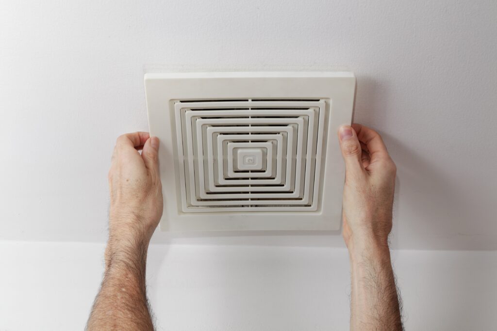 Man's hands removing air duct cover from ceiling